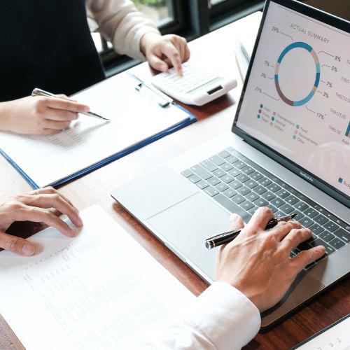 Two people work at a desk with a laptop displaying a financial chart, carefully planning their next investment. A notebook and calculator are within reach, all tools essential for the incubation stage of their business strategy.